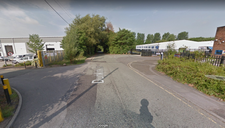 A Google Street View of an empty road with two industrial buildings flanking it.
